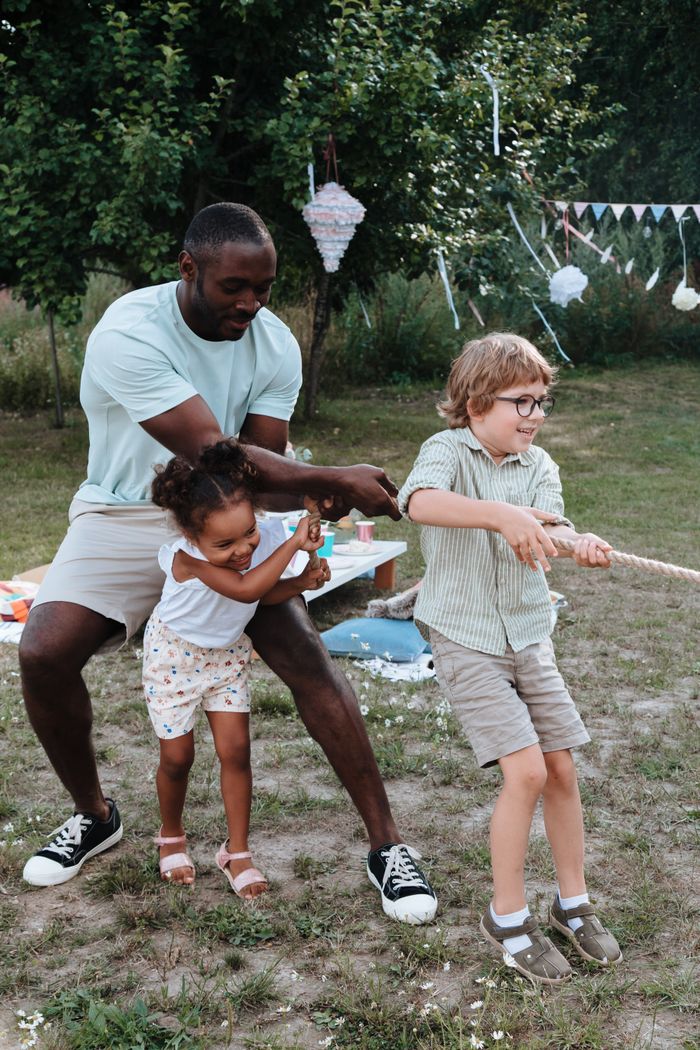 Services Father and children playing tug of war at a lively outdoor family gathering.