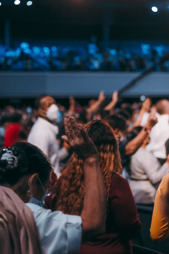 The Art of Drawing Readers In: Your attractive post title goes here A large indoor religious gathering with people wearing face masks and raising hands in worship.