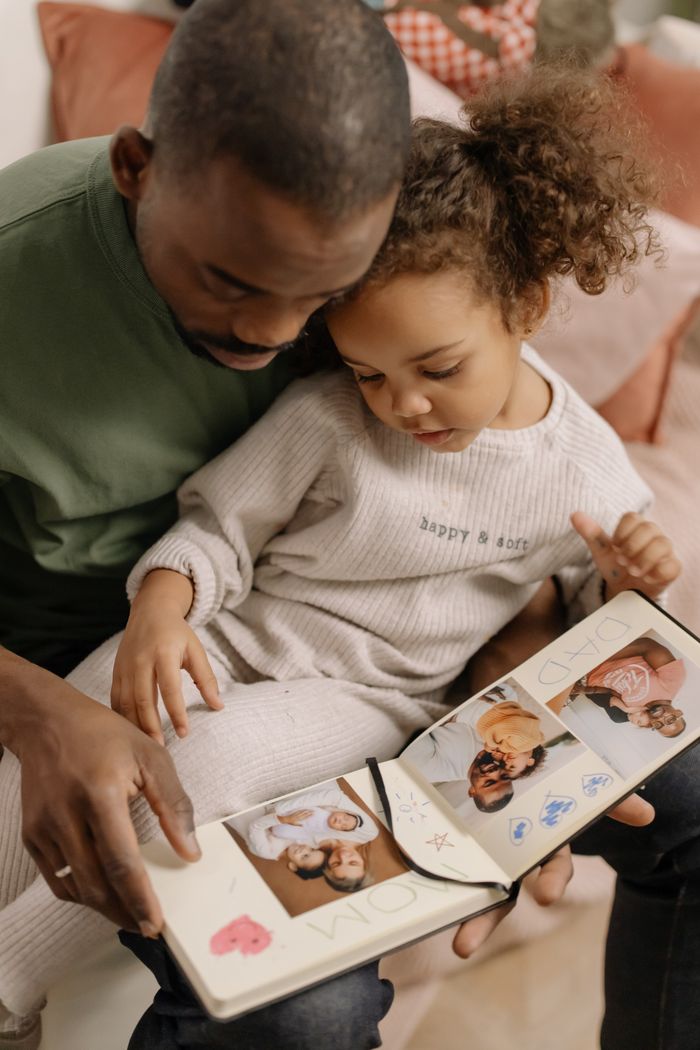 Services Black father and daughter enjoying a bonding moment with a photo album at home indoors.